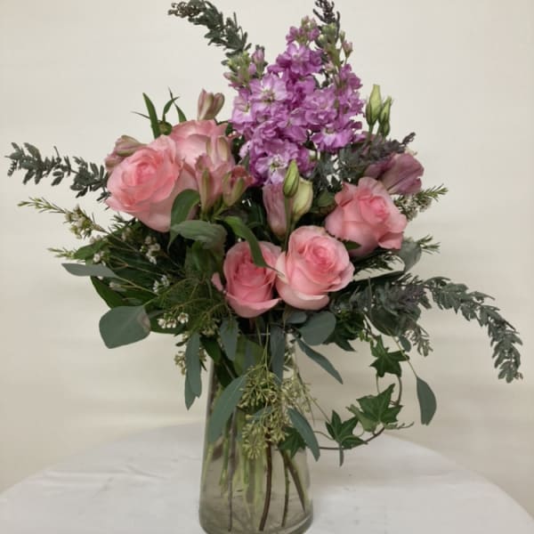 Pink roses and purple flowers arranged in a clear glass vase