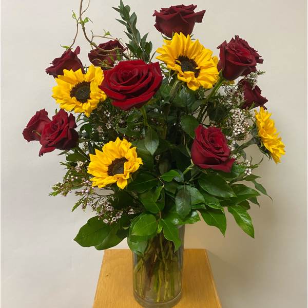 Bouquet of red roses and yellow sunflowers in a clear glass vase