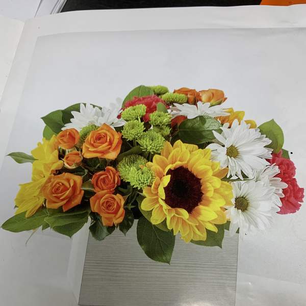 Mixed bouquet with sunflowers, orange roses, white daisies, and pink carnations in a box