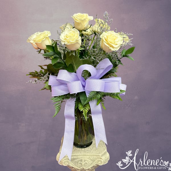 Yellow roses in a glass vase with a lavender ribbon bow