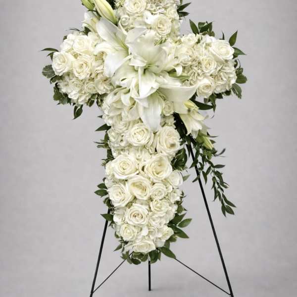 White floral cross on a black stand with lilies and roses