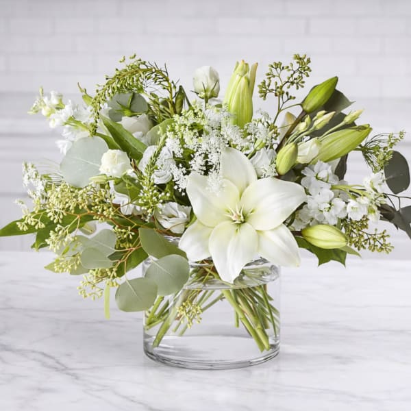 White lilies and mixed white flowers in a clear glass vase