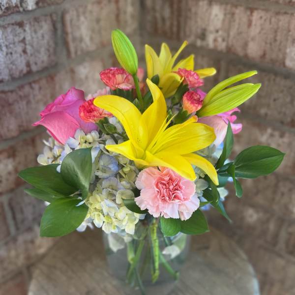 Bouquet of yellow lilies, pink roses, and carnations in a glass vase