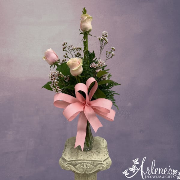 Pink and white roses in a glass vase with a large pink ribbon