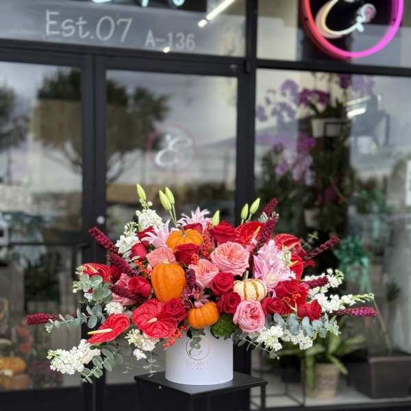 Large red and pink floral arrangement with small pumpkins in a white vase