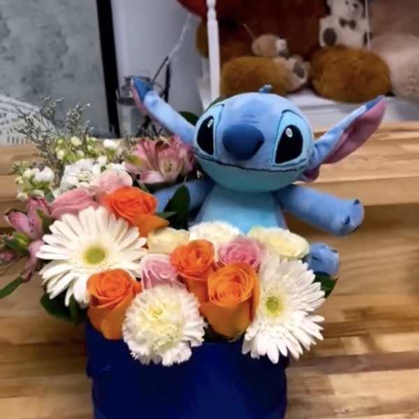 Blue plush toy in a box with orange and white flowers