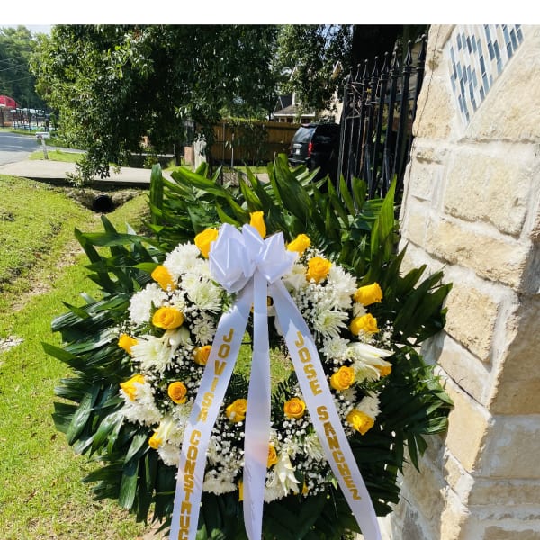 Standing wreath of yellow roses and white flowers with a white bow on an easel