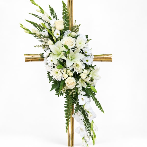 White floral cross arrangement with lilies, roses, and daisies on a bamboo cross