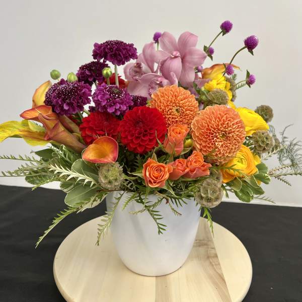Colorful mixed bouquet in a white vase with dahlias, orchids, roses, and calla lilies
