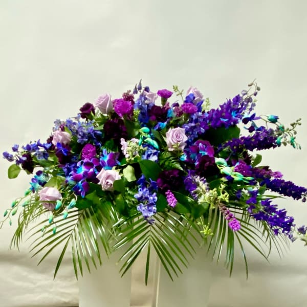 Large purple and blue floral arrangement in a white pedestal vase
