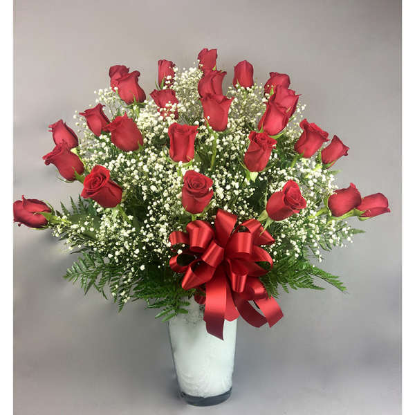 Red roses arranged in a clear vase with a red ribbon bow