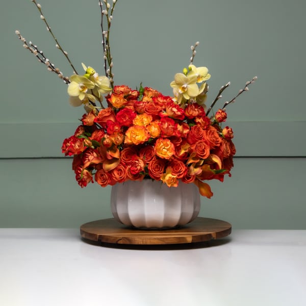 Orange and red floral arrangement in a white vase with tall branches