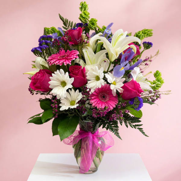 Mixed bouquet of pink roses, white lilies, and daisies in a glass vase