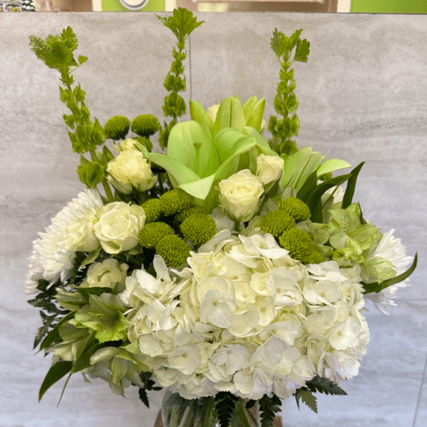 Tall white and green flower arrangement with hydrangeas and roses in a clear glass vase