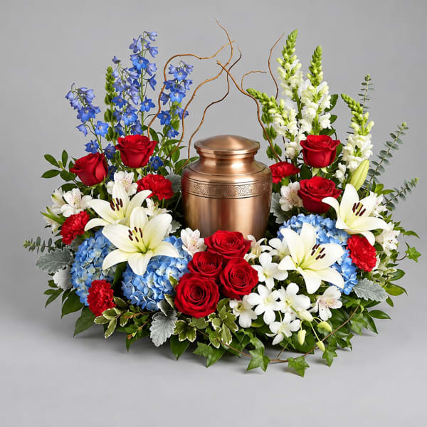 Floral funeral urn arrangement with red roses, white lilies, and blue flowers
