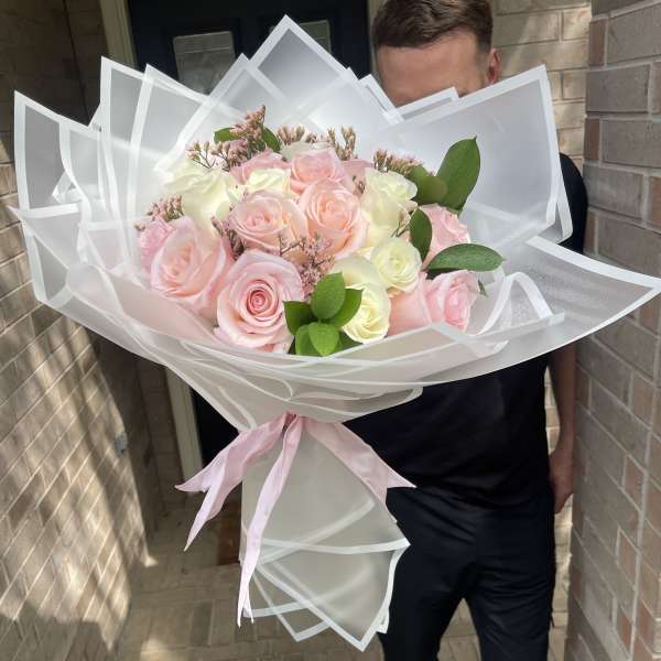 Large bouquet of pink and white roses wrapped in translucent paper