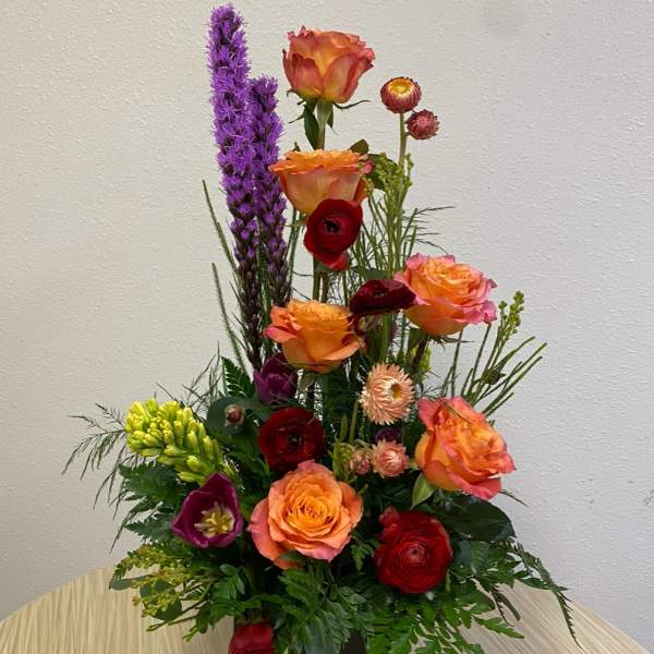 Tall mixed flower arrangement in a black square vase with orange and red blooms