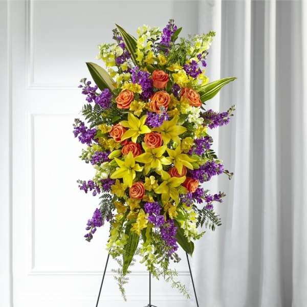 Standing spray of yellow lilies, orange roses, and purple flowers on a metal easel