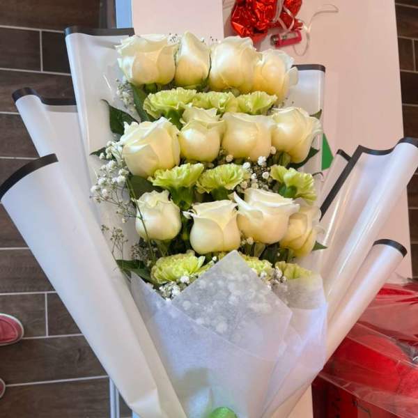 Bouquet of white roses and pale green carnations wrapped in white paper
