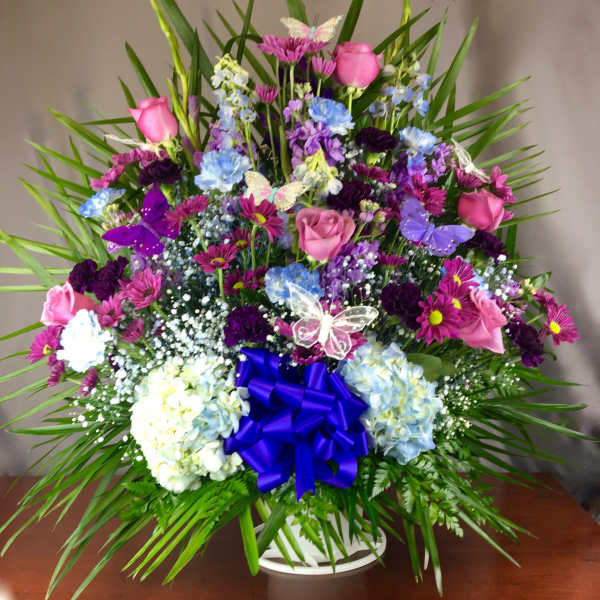 Colorful mixed flower arrangement in a white basket with a blue bow