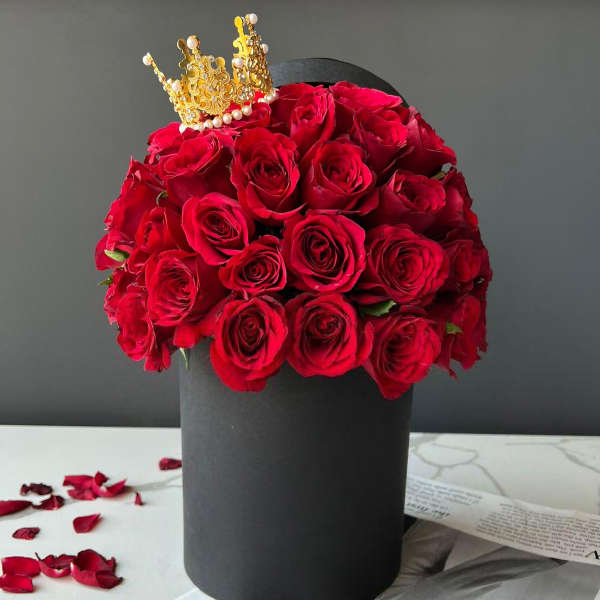 Red roses arranged in a black hat box with a gold crown topper