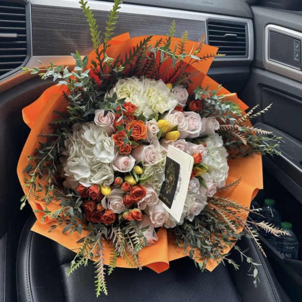 Mixed bouquet of roses and hydrangeas wrapped in bright orange paper