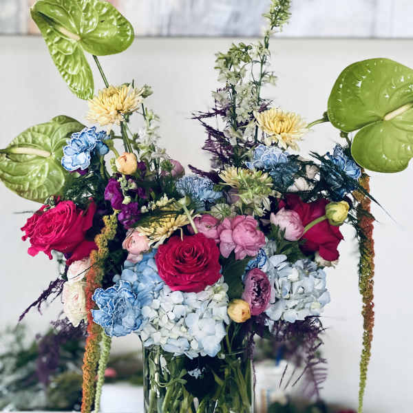 Colorful mixed bouquet in a clear glass vase with large green anthuriums