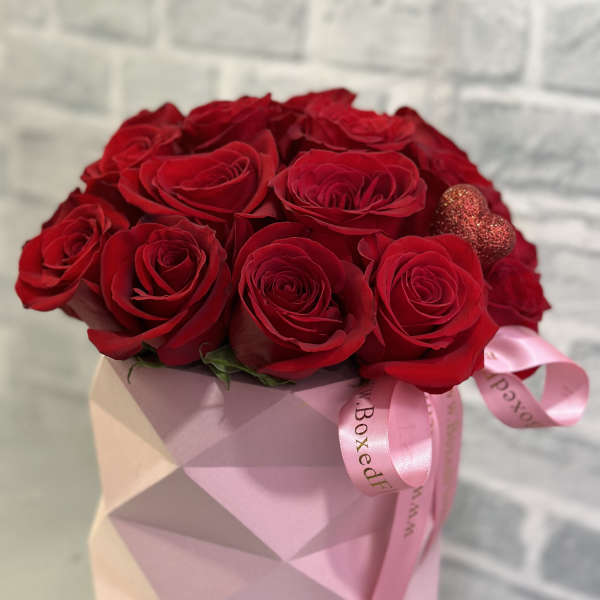 Red roses arranged in a pink geometric box with a ribbon