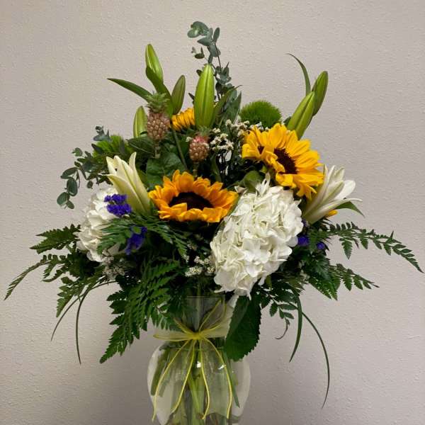 Bouquet of sunflowers, white lilies, and hydrangeas in a glass vase