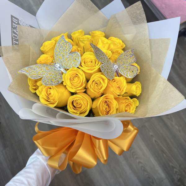 Bouquet of yellow roses wrapped in tan and white paper with silver butterfly picks