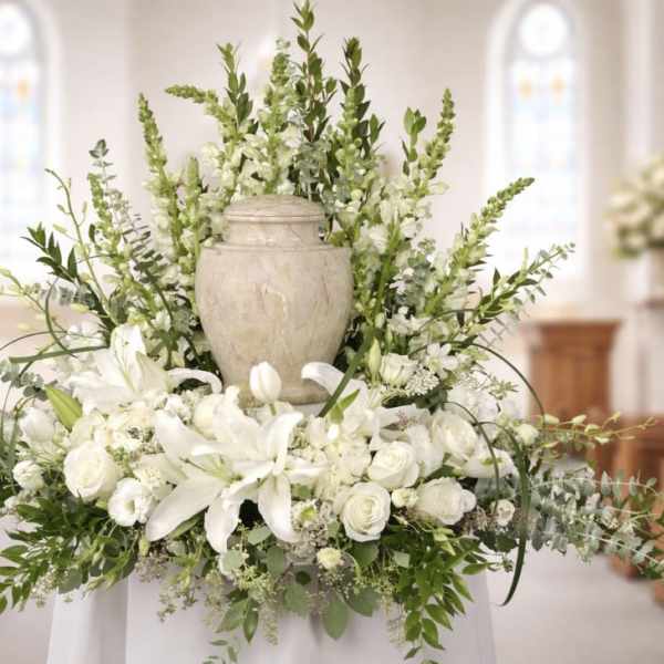 White floral arrangement with lilies and roses around a urn in a church setting