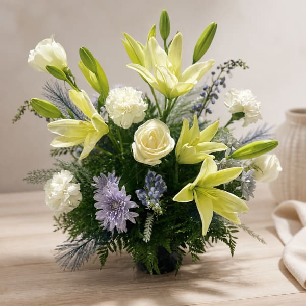 White lilies and roses arranged in a low vase with purple accents