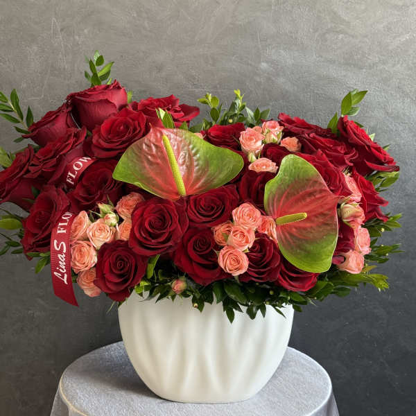 Red roses and peach spray roses in a white vase with anthuriums