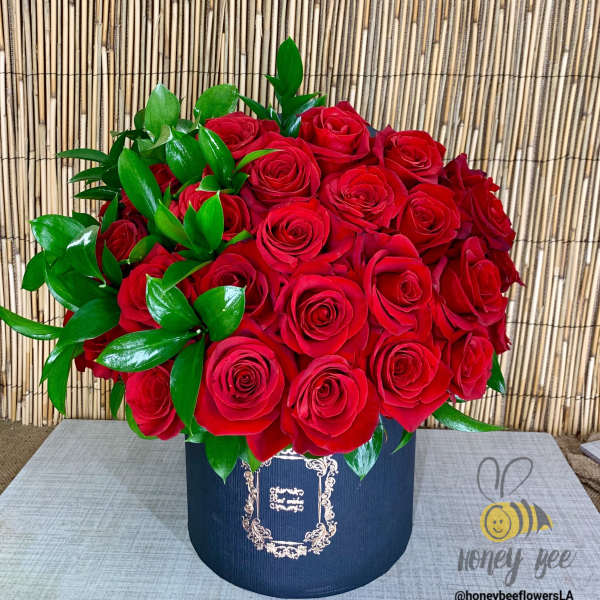 Red roses arranged in a navy hatbox with glossy green leaves