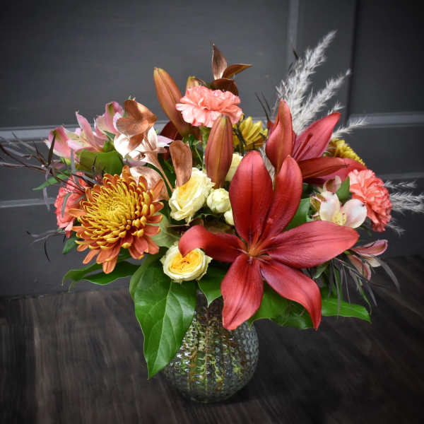 Mixed bouquet with red lilies, chrysanthemums, and roses in a glass vase