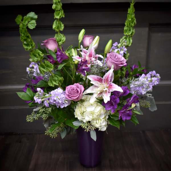 Purple and white floral arrangement in a tall vase