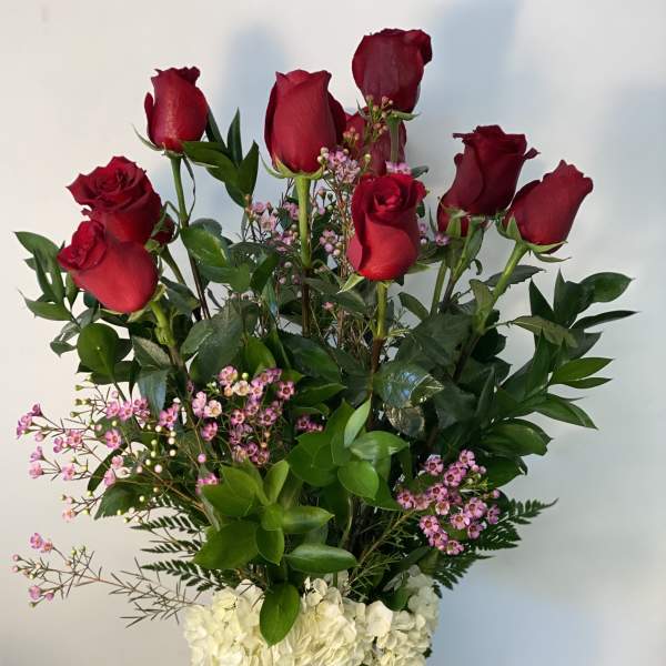 Tall vase arrangement of red roses, pink filler flowers, and white hydrangeas