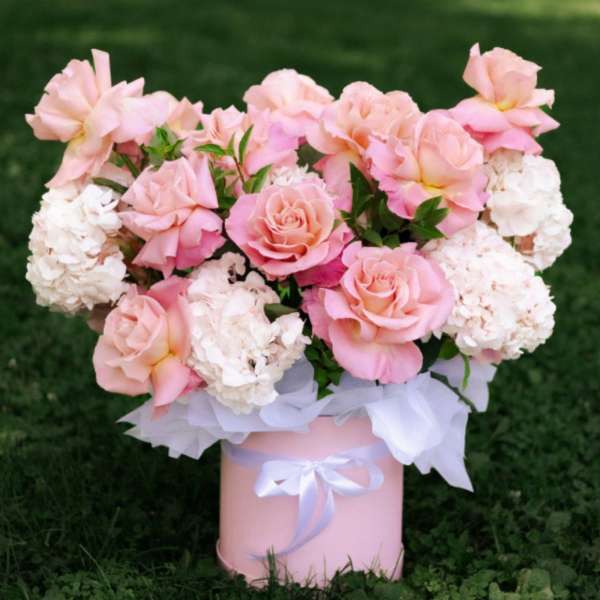 Pink roses and white hydrangeas arranged in a pink box with a white ribbon.