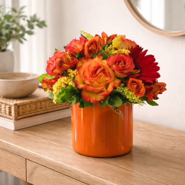 Compact bouquet of orange and red roses with yellow accents in an orange vase