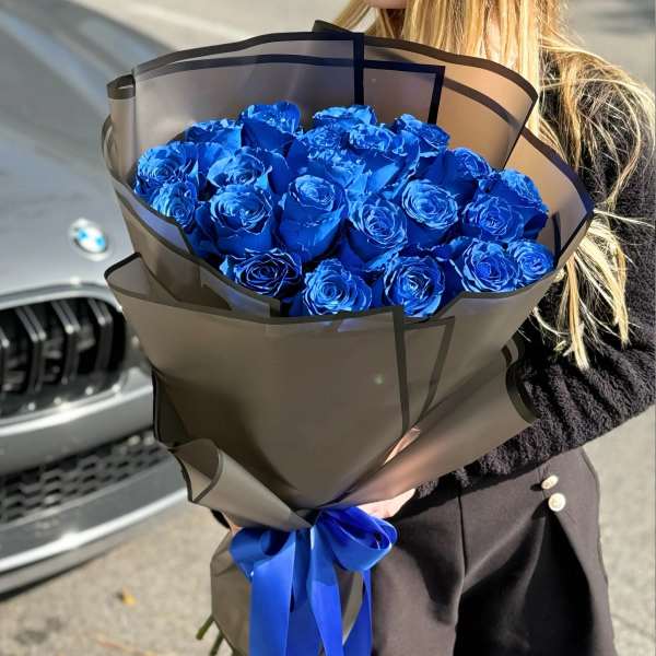 Bouquet of vivid blue roses wrapped in dark paper with a blue ribbon