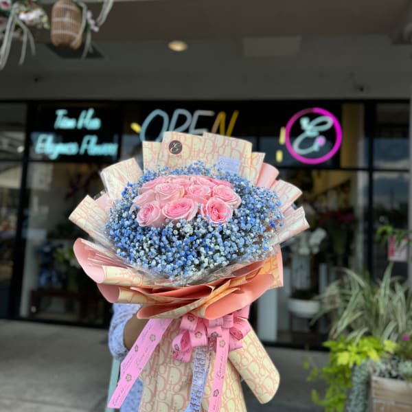 Pink roses in a large bouquet with blue filler flowers and pink wrapping