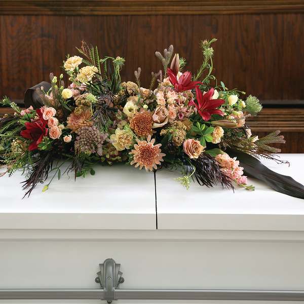 Large floral casket spray with red, peach, and cream blooms