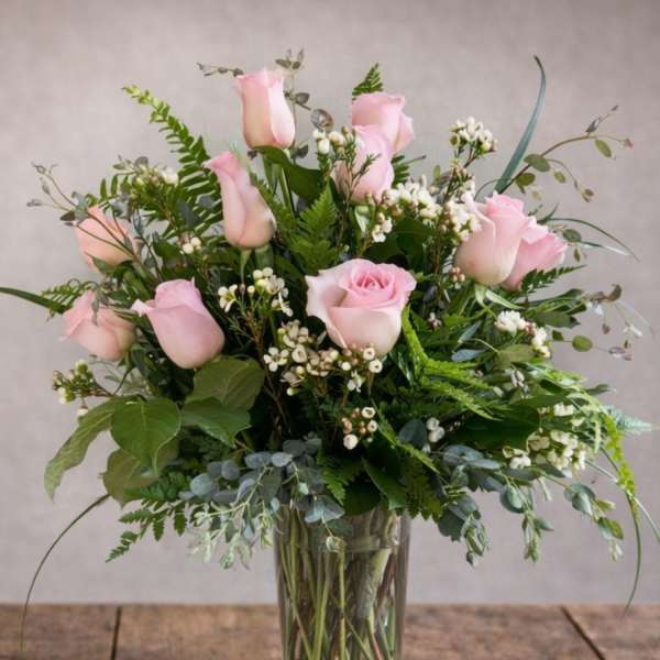 Pink roses arranged in a clear glass vase with mixed greenery.