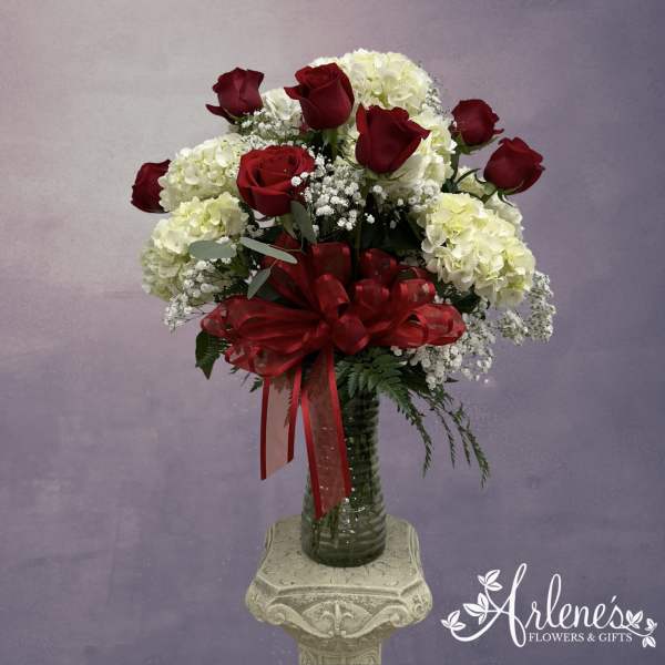 Red roses and white hydrangeas in a glass vase with a red ribbon