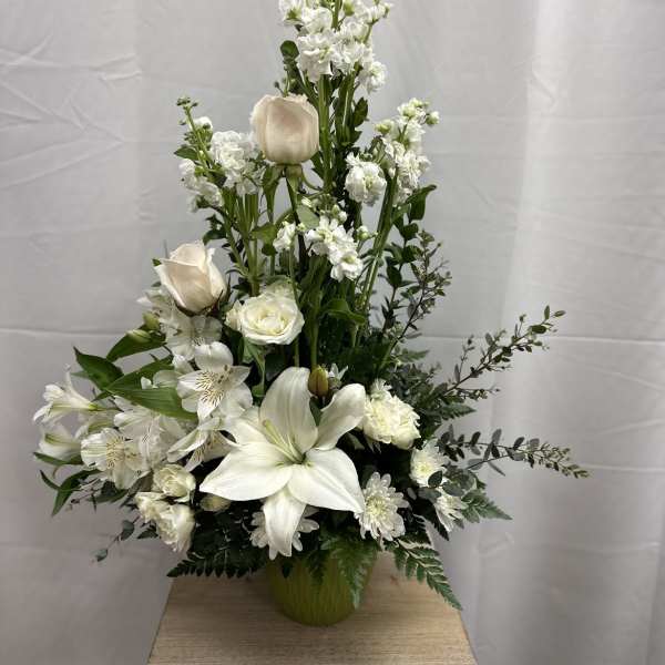Tall white floral arrangement in a green vase with lilies and roses