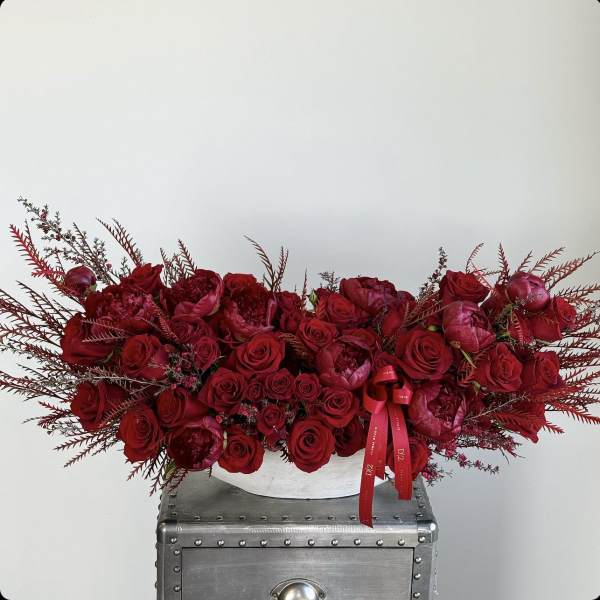 Long red rose arrangement in a white container with a red ribbon