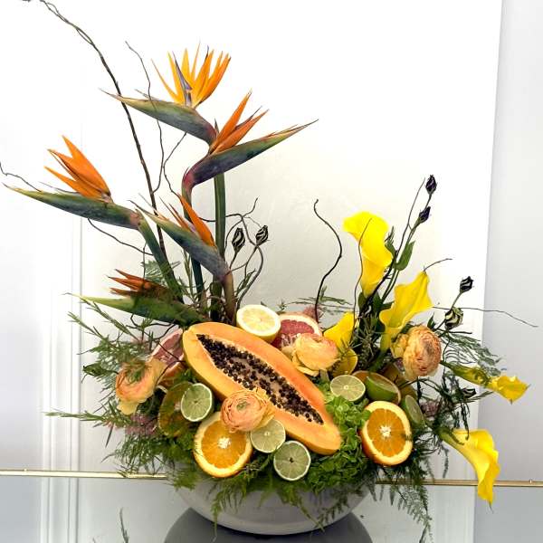 Tropical floral arrangement with bird of paradise, calla lilies, and sliced fruit in a bowl