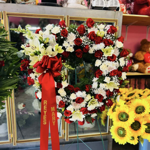 Heart-shaped floral wreath of red and white flowers on a stand with a red ribbon
