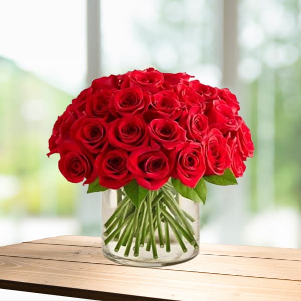 Red rose bouquet in a clear glass vase on a wooden table