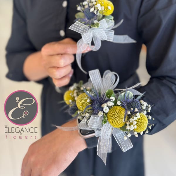 Two small floral boutonnieres with yellow and blue blooms and silver ribbon